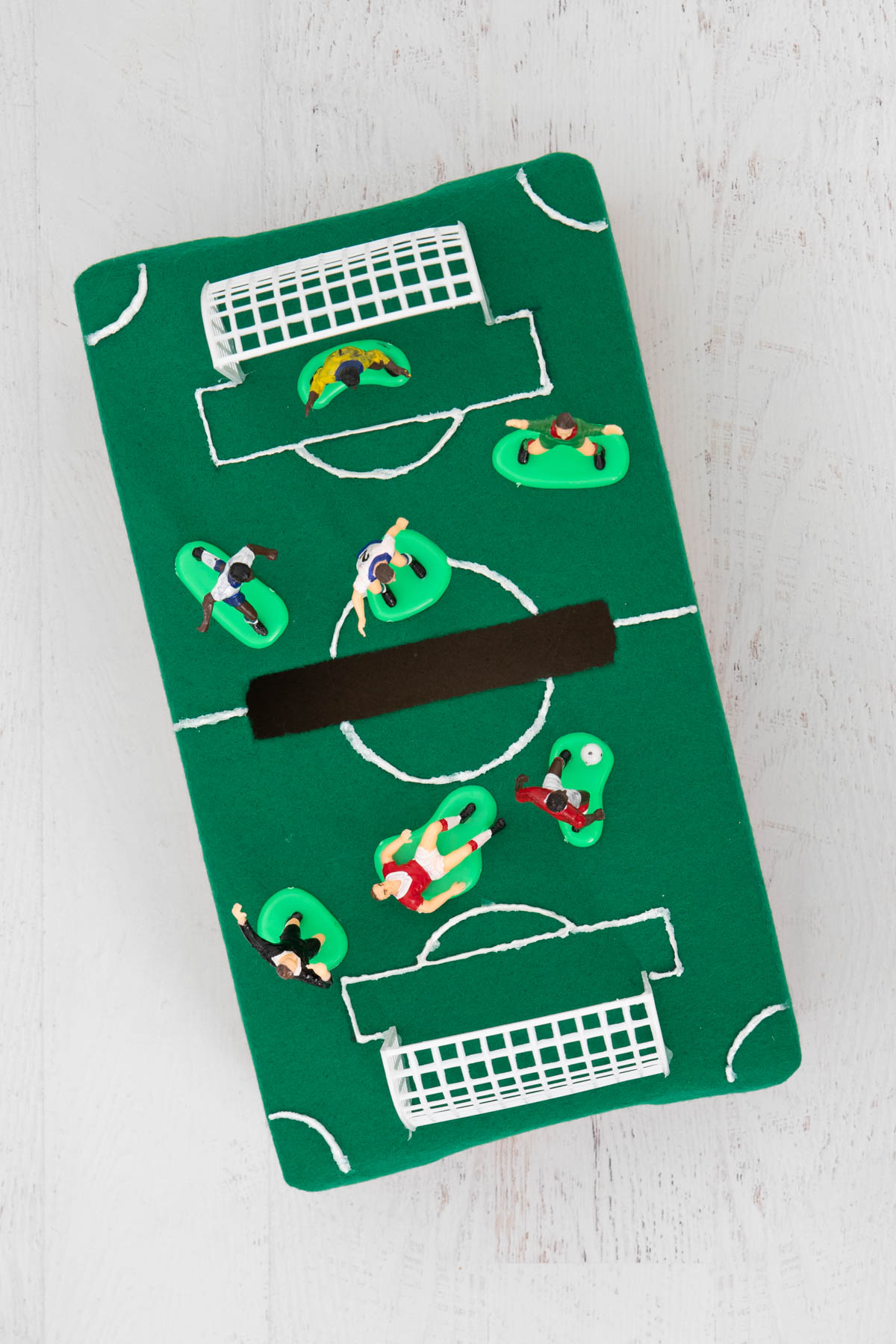 A small box decorated like a soccer field with toy people on it.
