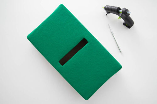A green felt box with a hole cut in it next to a glue gun