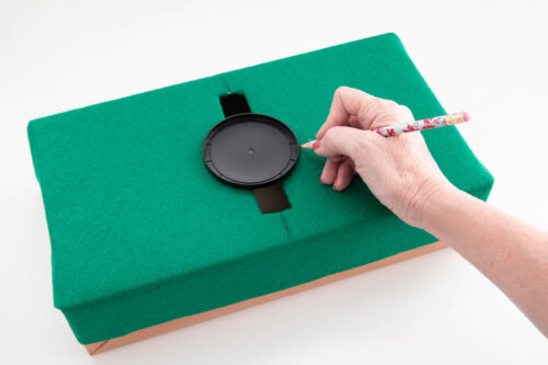 A person is using a pencil to draw on a green box.