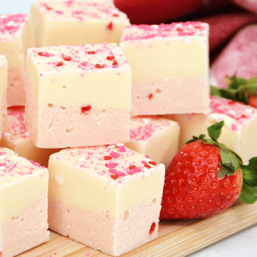 Pink and white fudge with strawberries on a wooden cutting board.
