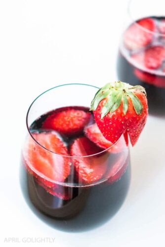 Two glasses of red wine with strawberries in them.
