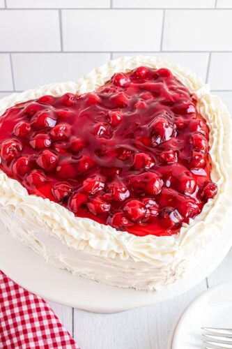 A heart shaped cake with cherries on top.