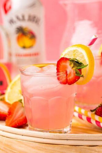 A pink drink with strawberries and lemons on a tray.