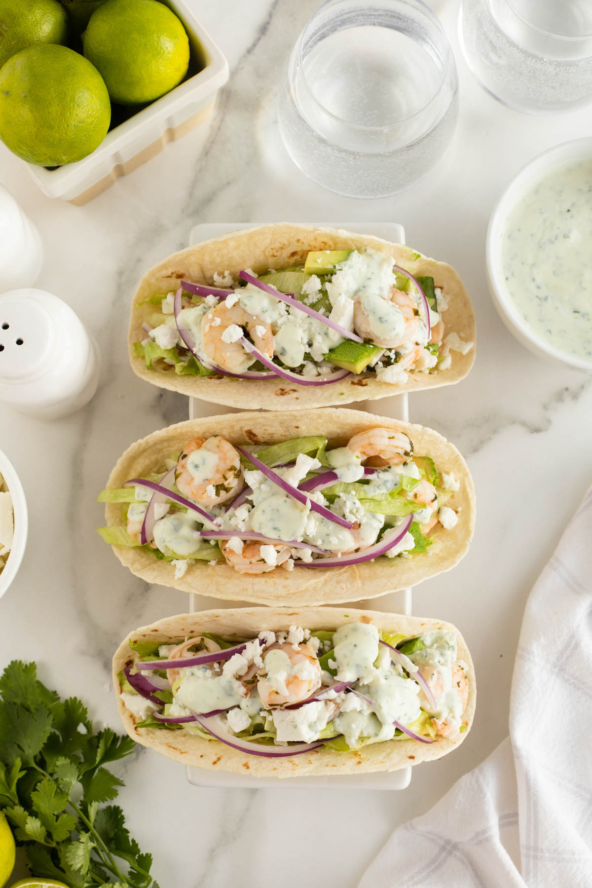 A group of shrimp tacos with sauces and vegetables.