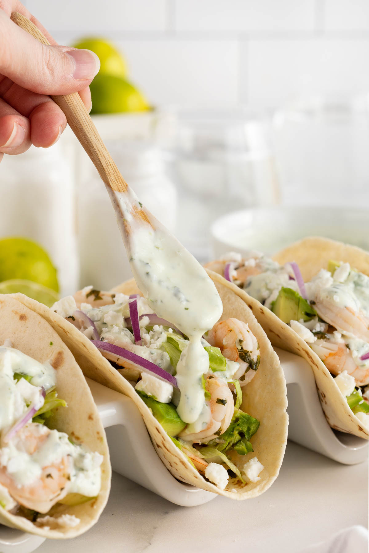 A person is drizzling cilantro lime sauce over shrimp tacos.