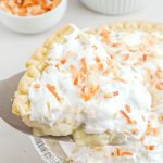A slice of coconut cream pie with whipped cream and coconut shavings.