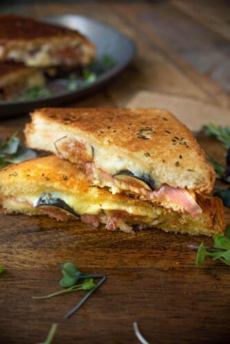 A grilled sandwich with ham and cheese on a wooden board.