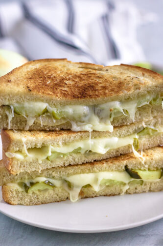 A grilled cheese sandwich with pickles and cheese on a plate.