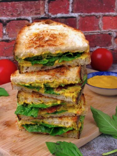 A stack of grilled sandwiches on a wooden cutting board.