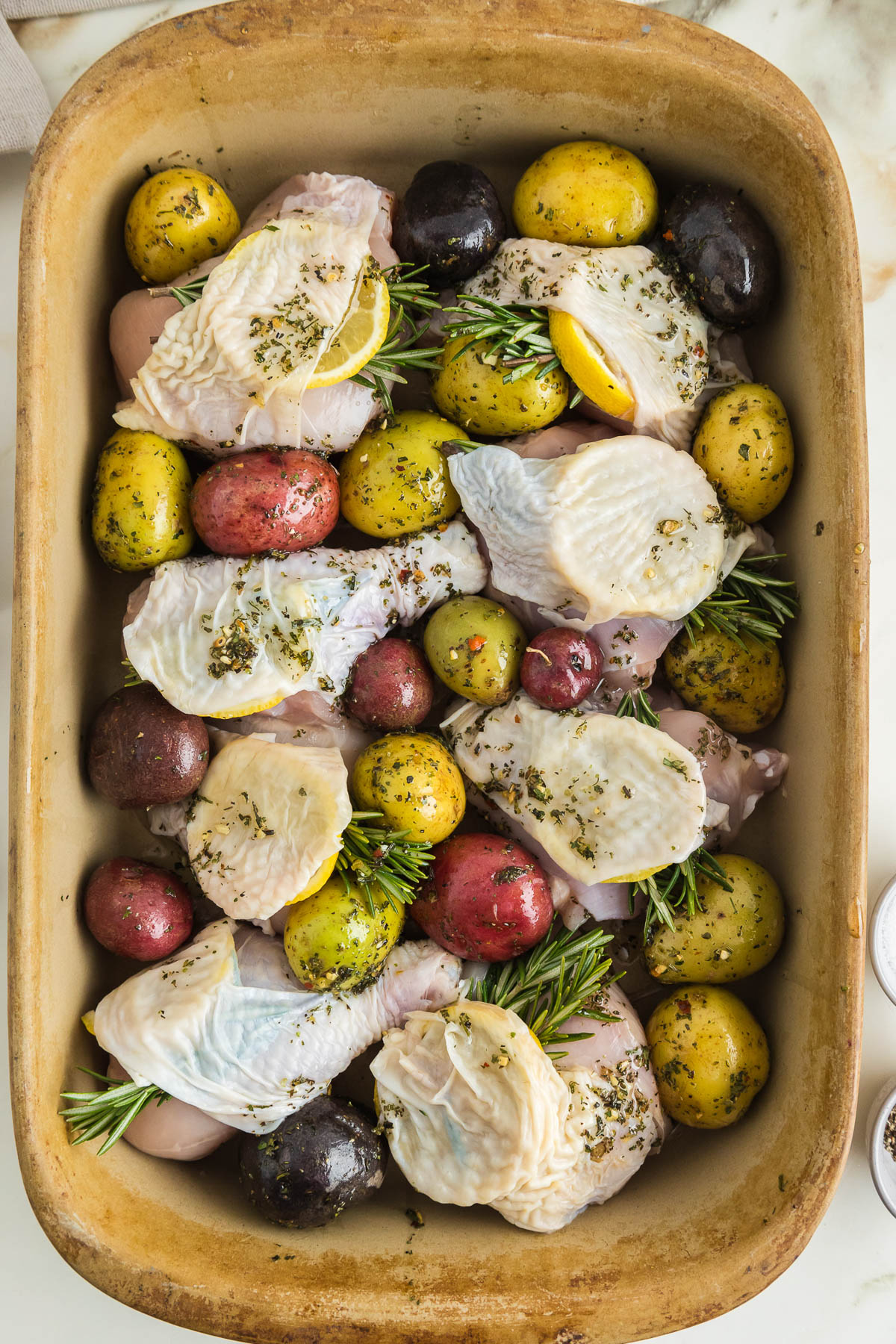 Chicken with potatoes and rosemary in a baking dish.