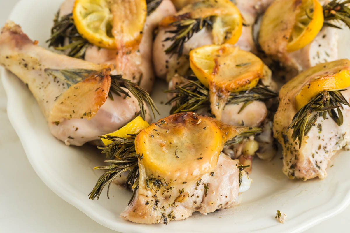 Roasted chicken with rosemary and lemons on a white plate.