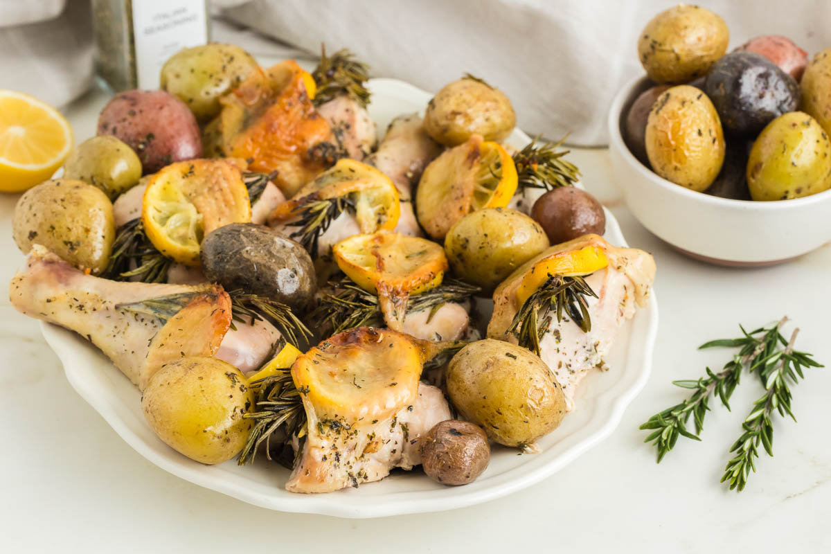 Roasted chicken with potatoes and rosemary on a white plate.