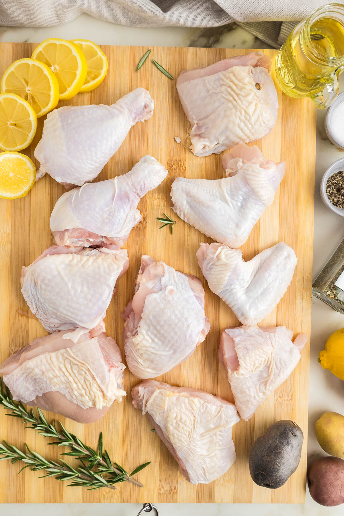 Chicken breasts on a cutting board with lemons and herbs.