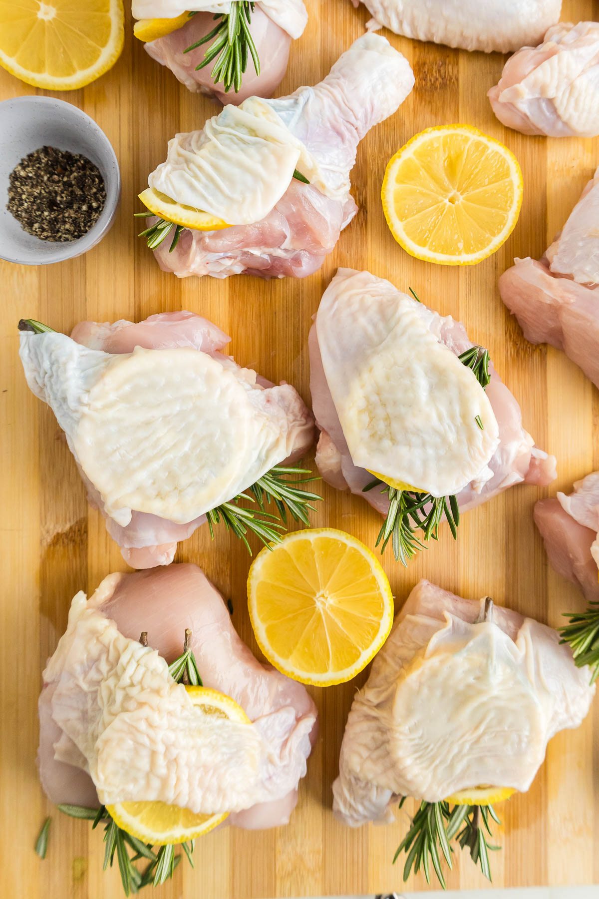 Chicken with rosemary and lemon slices on a cutting board.