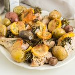 Roasted chicken with potatoes and lemons on a plate.