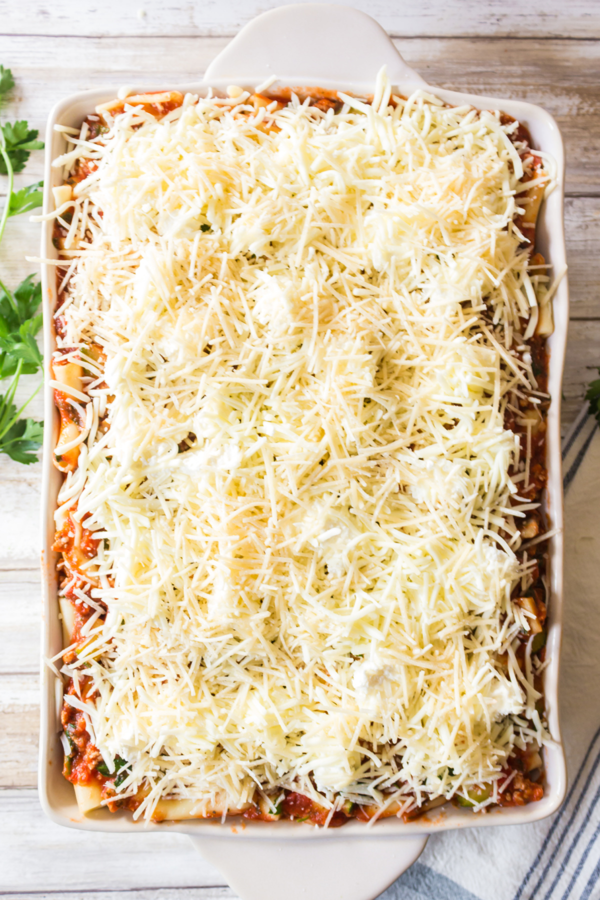 An unbaked ziti dish topped with shredded cheese in a white casserole dish.