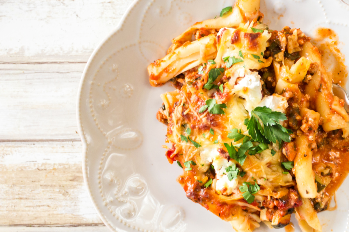 A plate of baked ziti garnished with herbs on a wooden table.