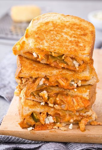A grilled cheese sandwich with buffalo chicken and melted cheese, sliced and stacked on a wooden board.