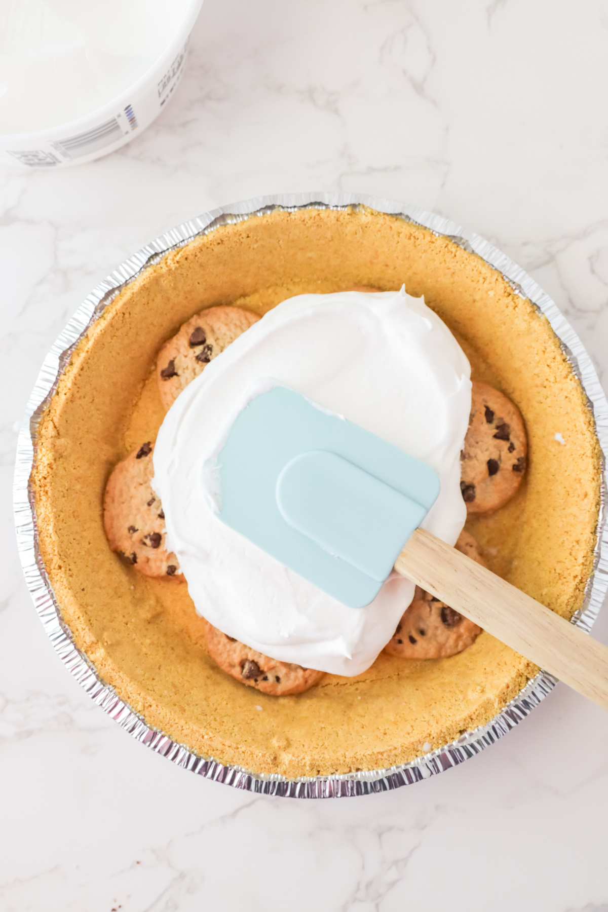 Spreading whipped cream onto a cookie pie crust with a spatula.