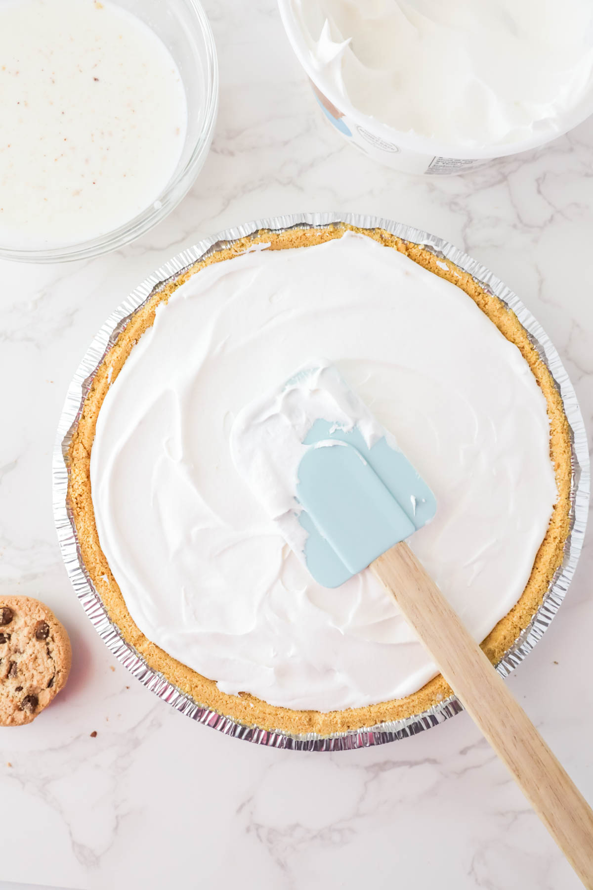 Spreading whipped cream on a pie crust with a spatula.