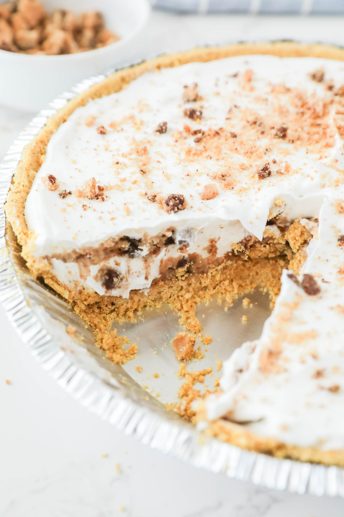 A sliced cream pie with a crumbly crust and a topping of whipped cream and crumbled pieces.