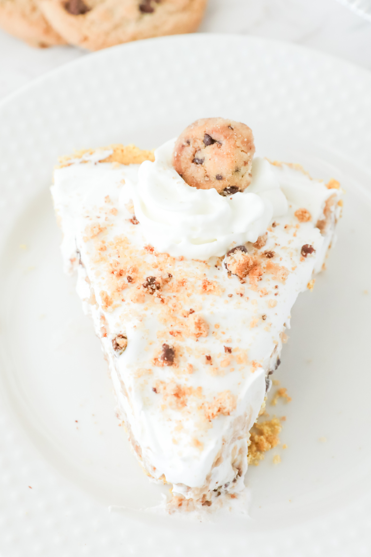 A slice of cool whip cookie pie topped with whipped cream and a mini cookie on a white plate.