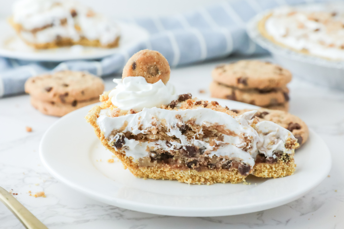 A slice of cookie pie topped with whipped cream on a white plate, with more cookies in the background.