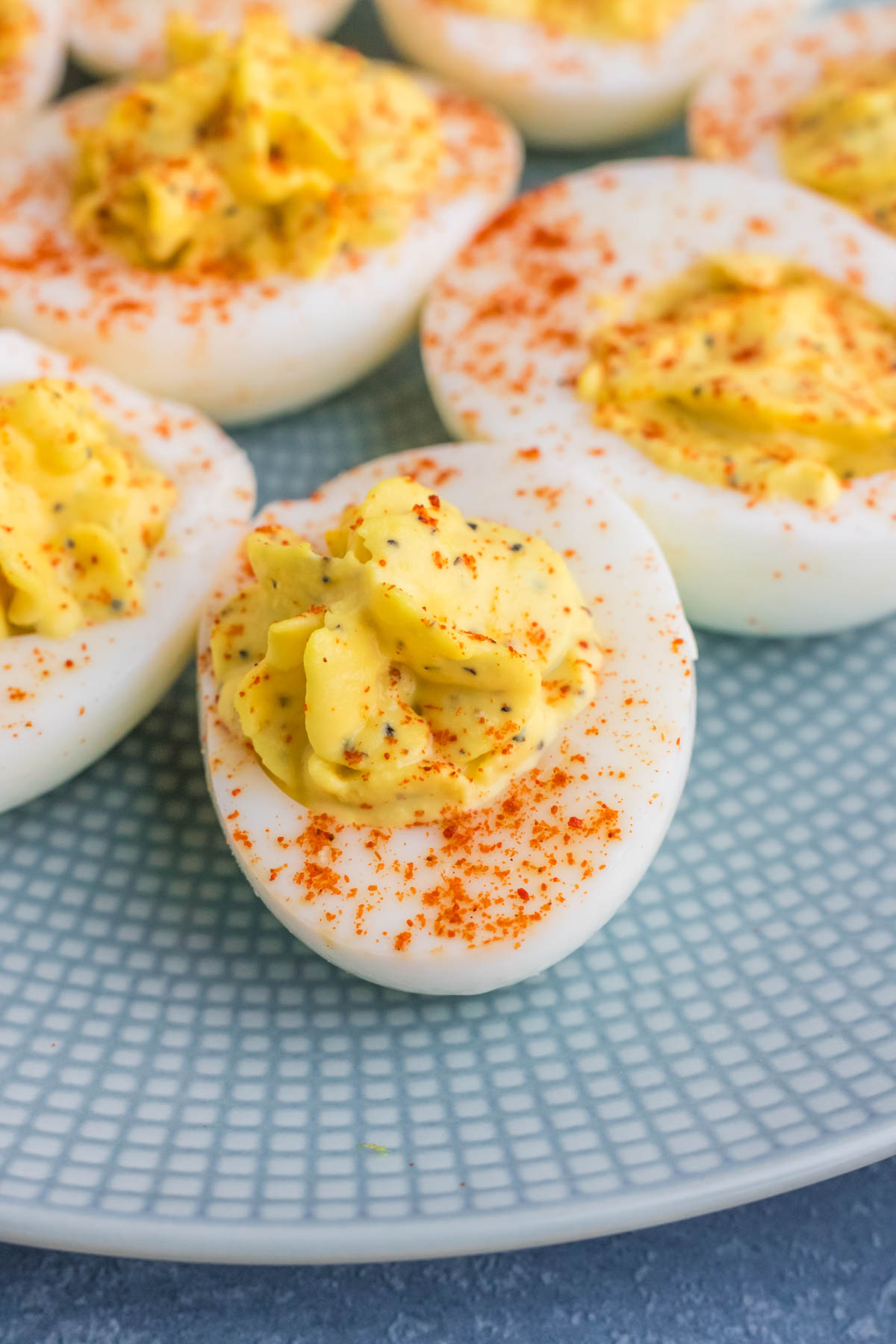 Deviled eggs sprinkled with paprika served on a blue plate.