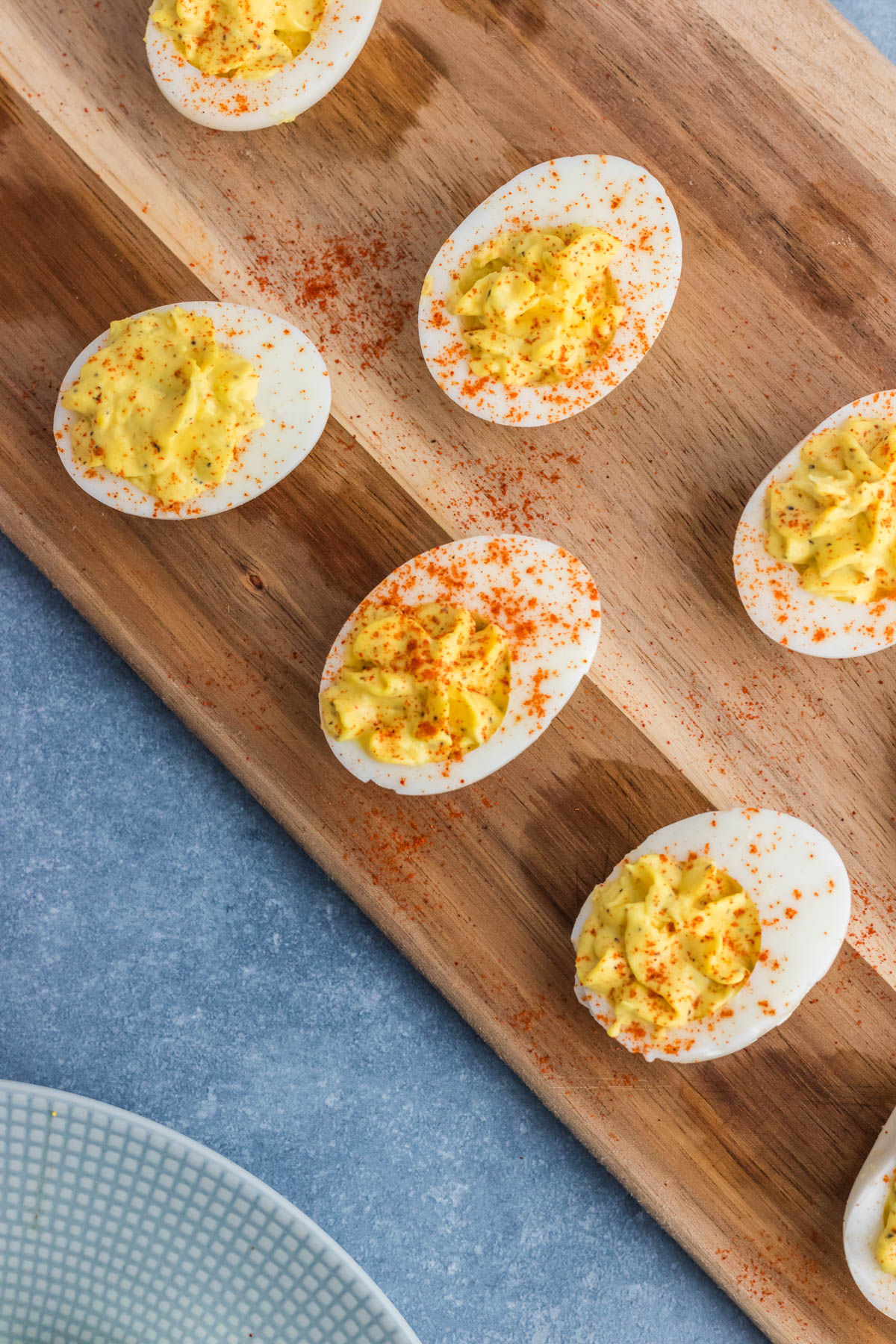 Deviled eggs sprinkled with paprika on a wooden serving board.