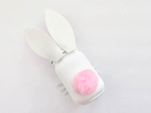 White mason jar with bunny ears and a pink fluffy tail on a white background.