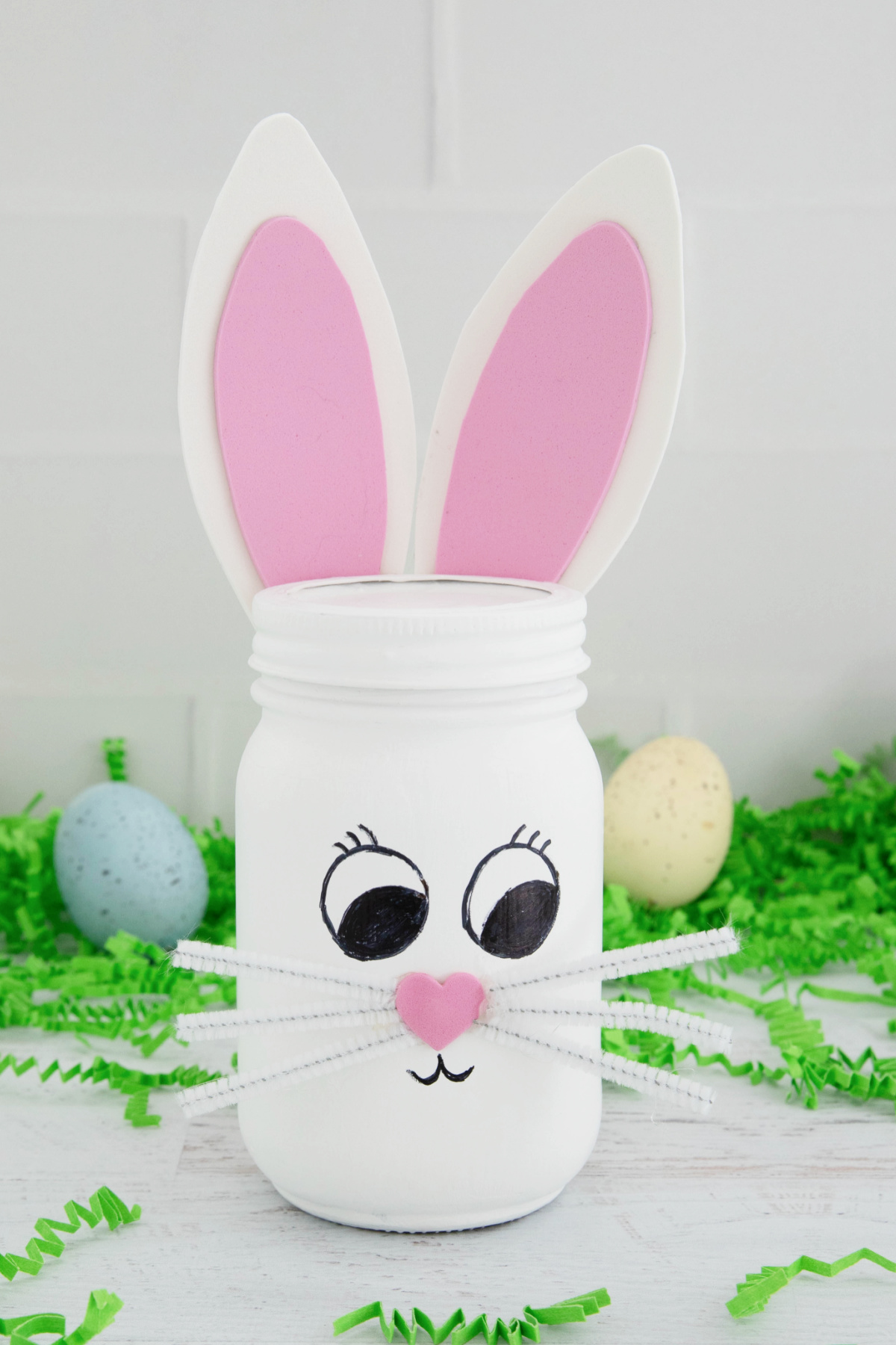 A decorative jar painted to look like a bunny with pink ears and a face, accompanied by easter eggs in the background.