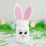 A decorated jar with bunny ears and face, set amid easter decorations.