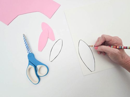 A person tracing oval shapes on paper next to cut-out pink paper ovals and a pair of scissors.