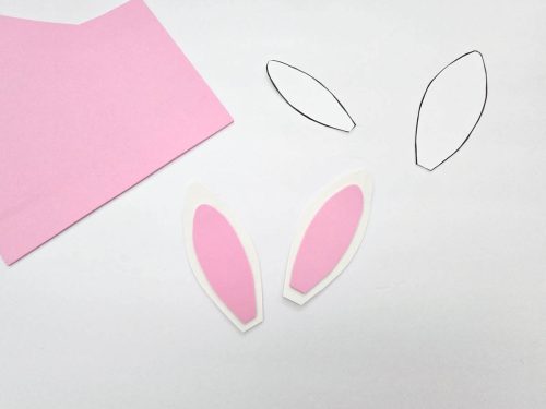 Paper cutouts for bunny ears crafts with templates and pink construction paper on a white surface.
