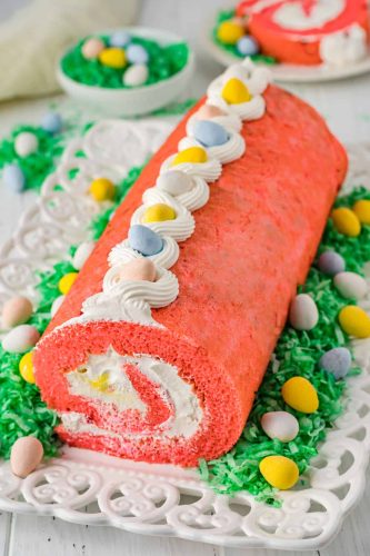 Easter roll cake with icing and easter eggs on a plate.