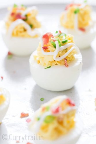 Deviled eggs topped with bacon bits and garnished with chives on a white surface.