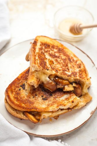 Grilled cheese sandwich with mushrooms on a plate, served with a side of honey.