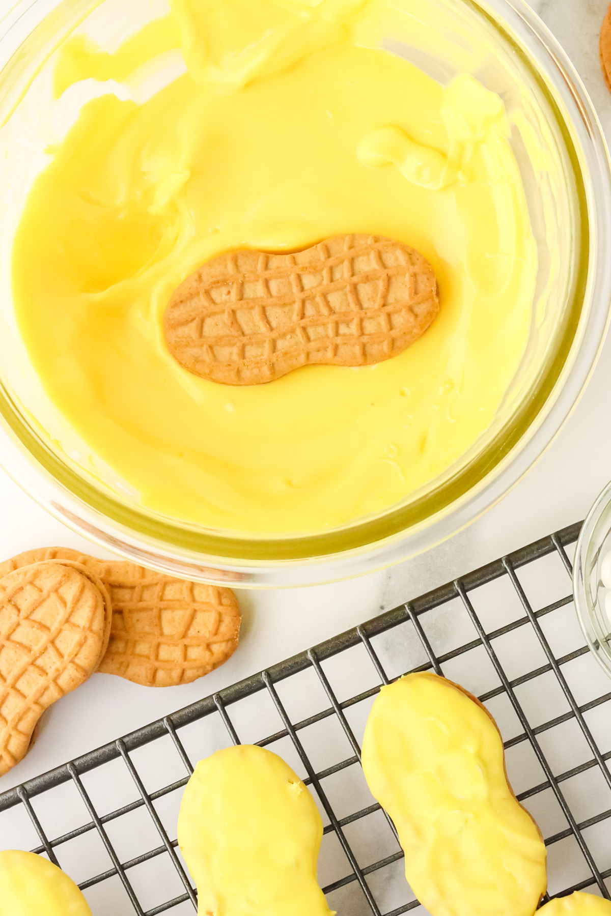 Cookies being dipped in yellow chocolate and placed on a cooling rack.