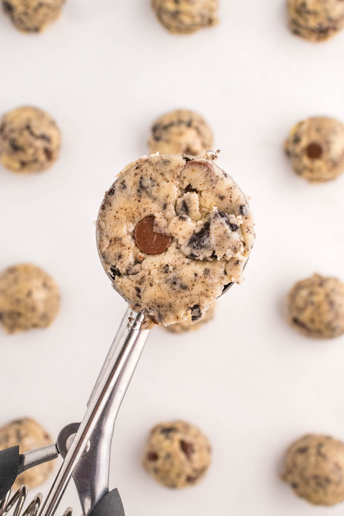 A cookie scoop containing raw oreo cake mix cookie dough, with more dough balls in the background.