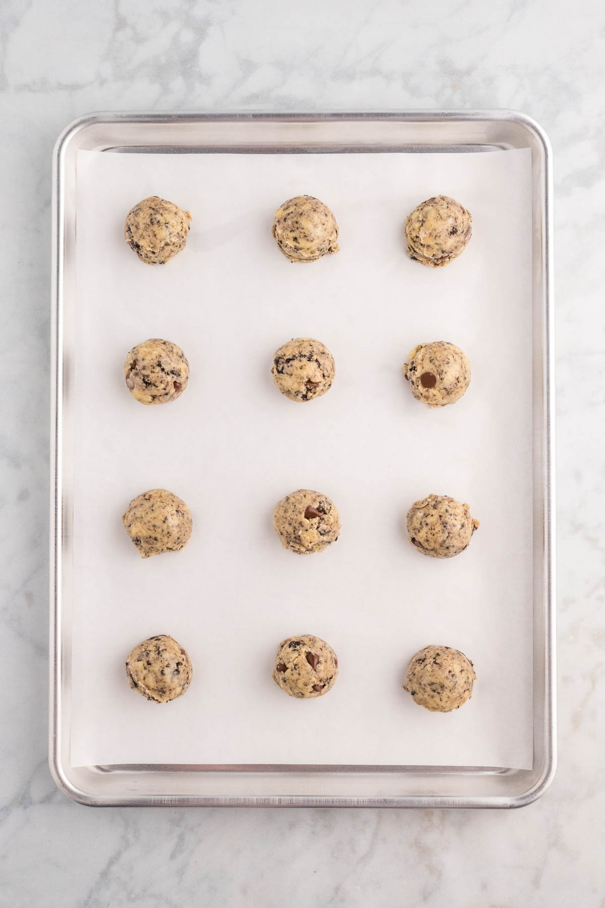 Raw cookie dough balls evenly spaced on a baking sheet lined with parchment paper.