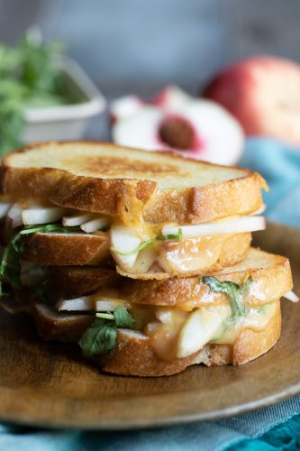Grilled cheese sandwich with apple slices and greens on a wooden plate.