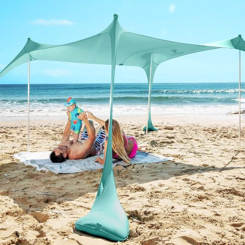 A family relaxing under a portable sunshade on a sandy beach.