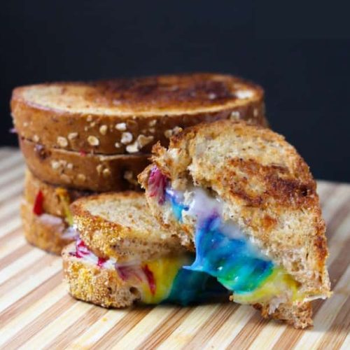 Grilled cheese sandwich with multicolored melted cheese on a wooden board.