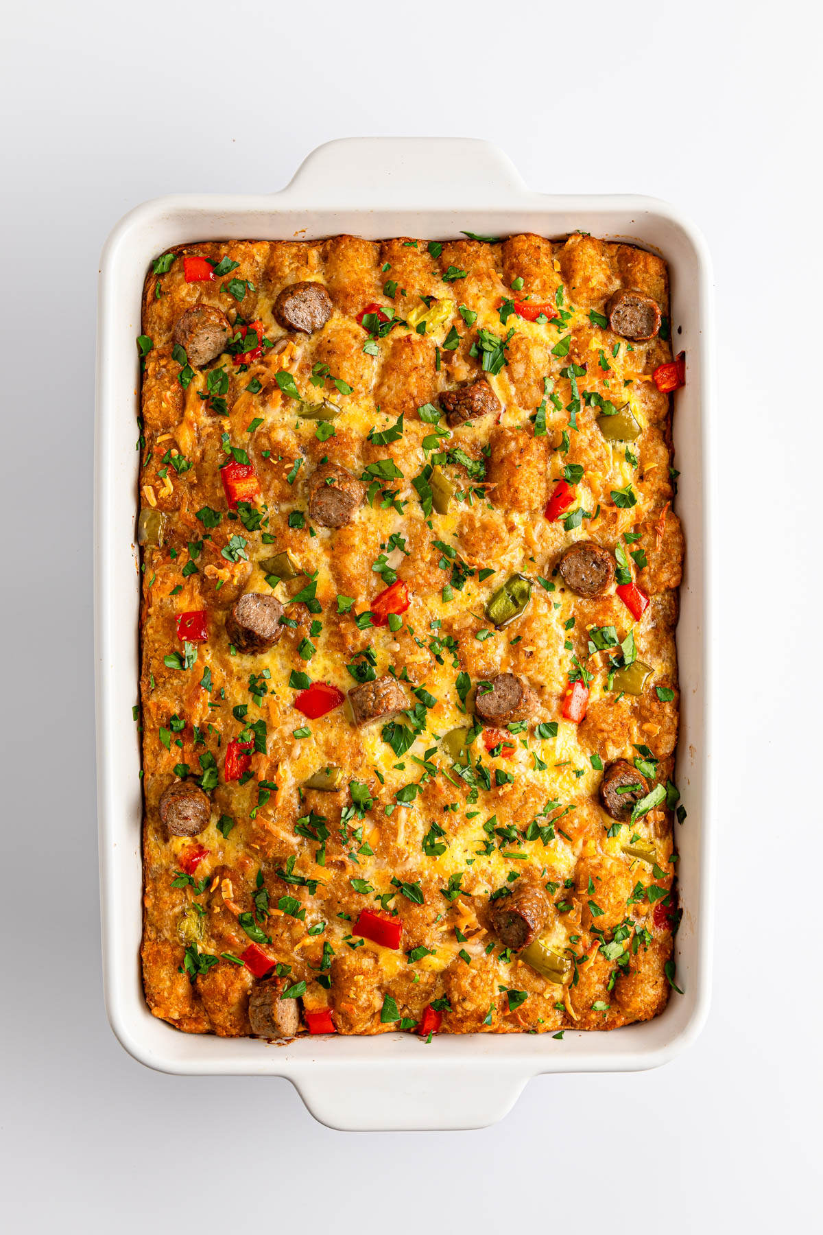 A freshly baked casserole with vegetables and sausage in a white baking dish.