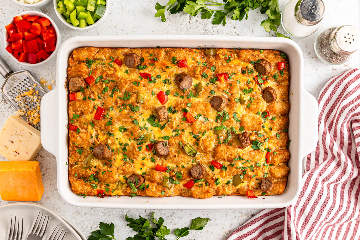 A freshly baked casserole with sausage, vegetables, and cheese, garnished with herbs on a kitchen counter.