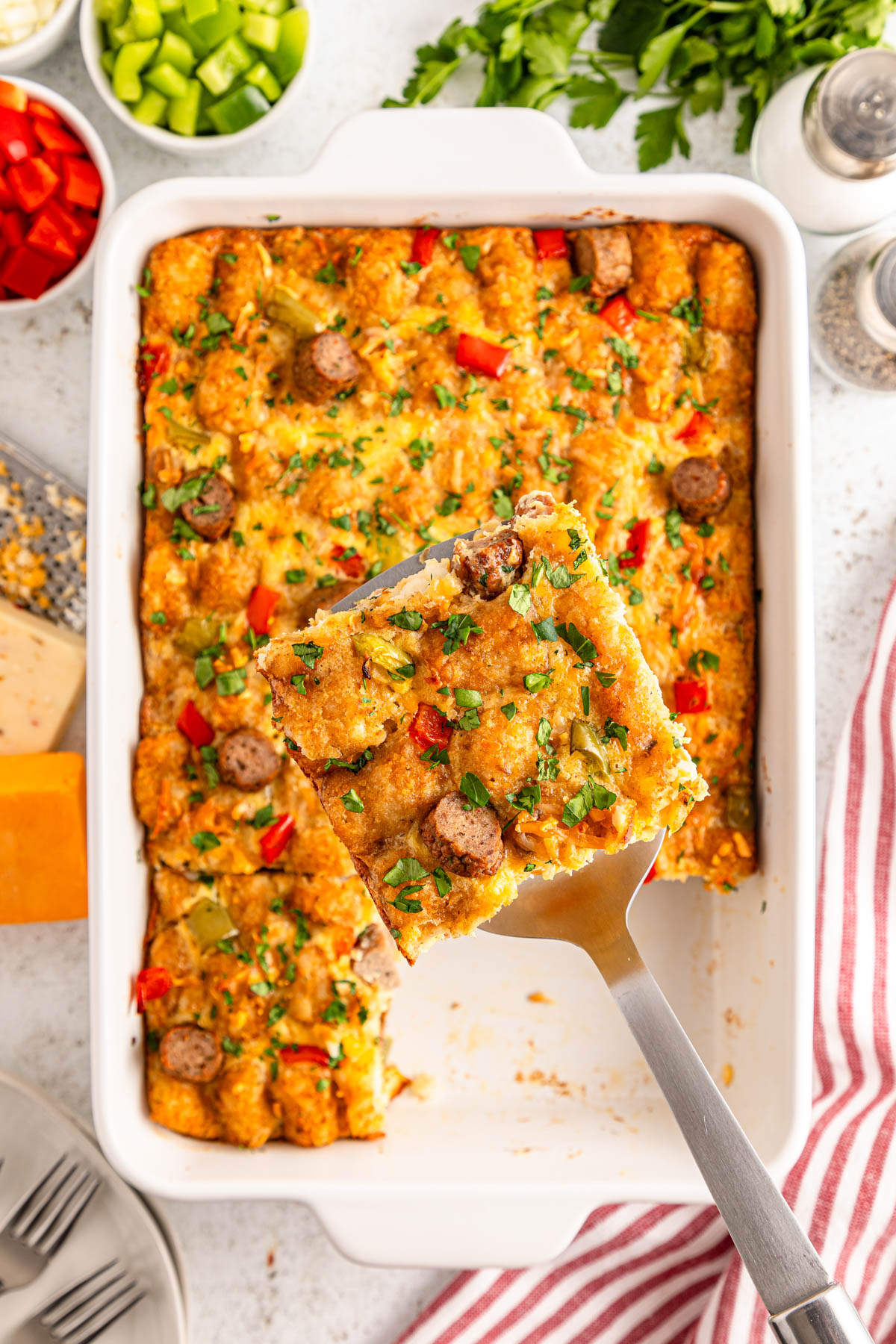 A freshly baked casserole with sausage, cheese, and diced vegetables, served with a spatula.