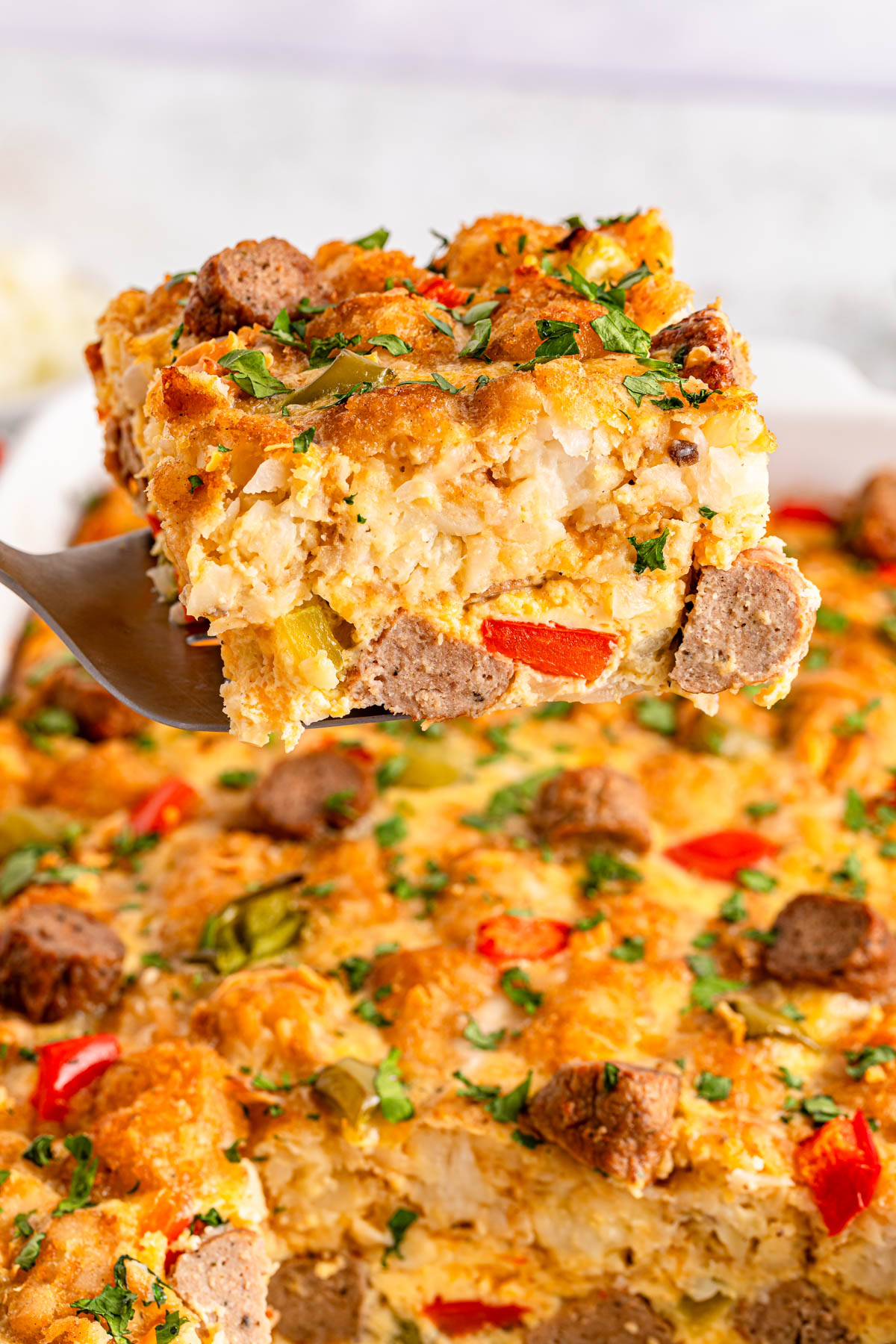 A slice of savory breakfast casserole with sausage, peppers, and eggs being lifted on a spatula.