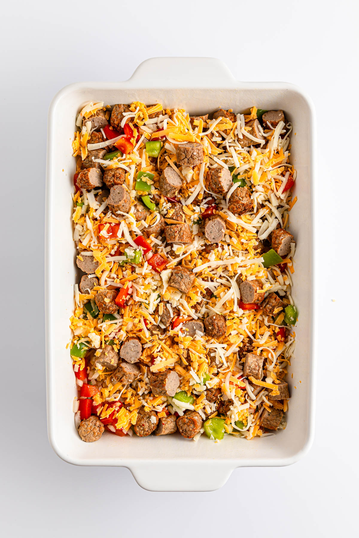 A baking dish filled with a colorful sausage and vegetable casserole topped with shredded cheese.