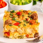 A slice of sausage and tater tot casserole garnished with fresh herbs on a plate.