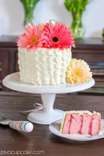 A pink cake on a white plate with flowers on it.